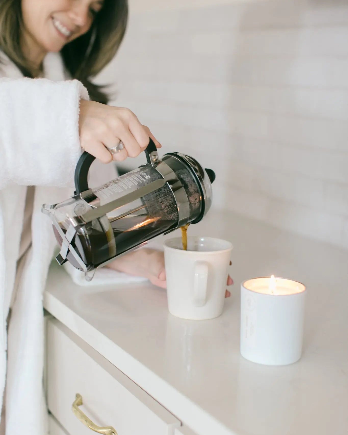 Woman pouring coffee in a mug with a candle burning nearby