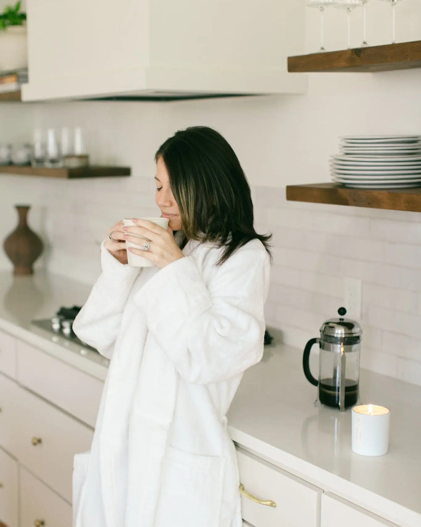 woman smelling a cup of coffee with a candle burning nearby
