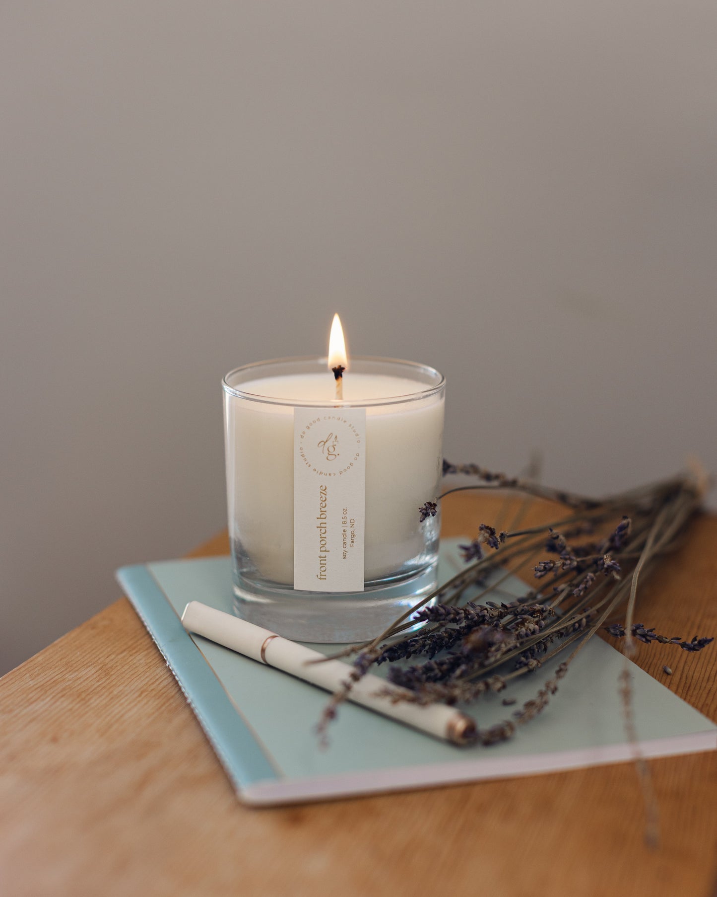 Front Porch Breeze candle burning while sitting on a blue journal with a pen and sprig of lavender