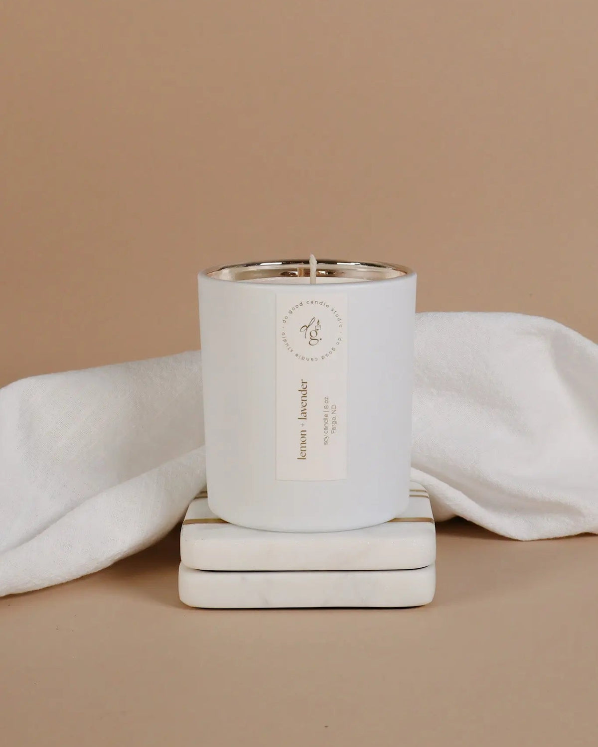 Lemon + Lavender cnandle styled on a beige backdrop with white coasters and a white linen cloth