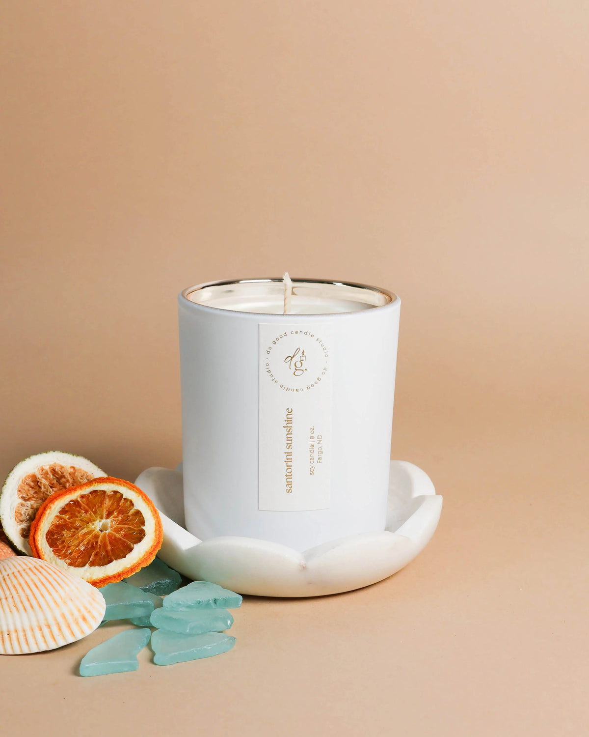 White candle in a decorative holder with orange slices and seashells on a beige background