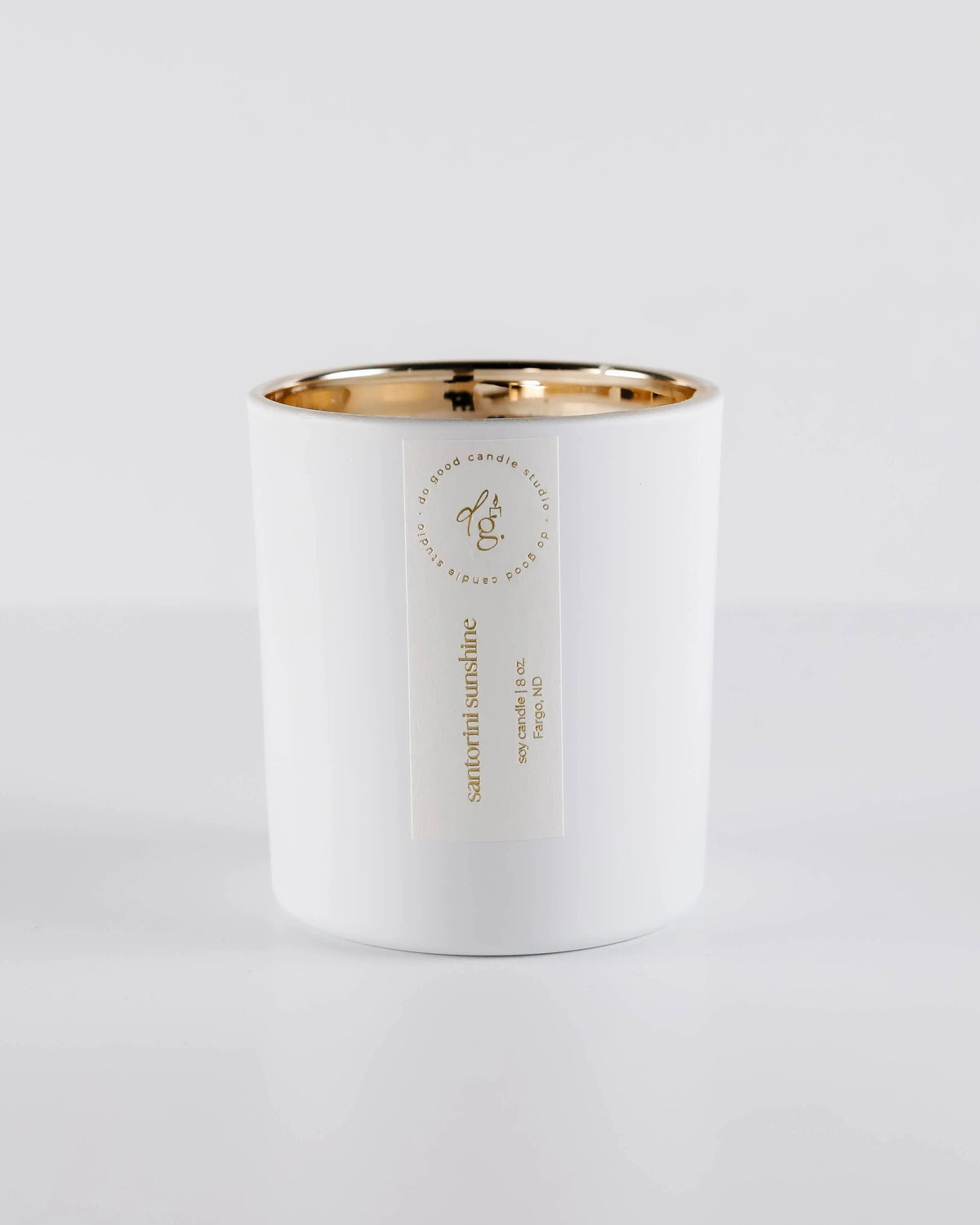 Soy candle in matte white vessel with gold interior and label on a light gray background