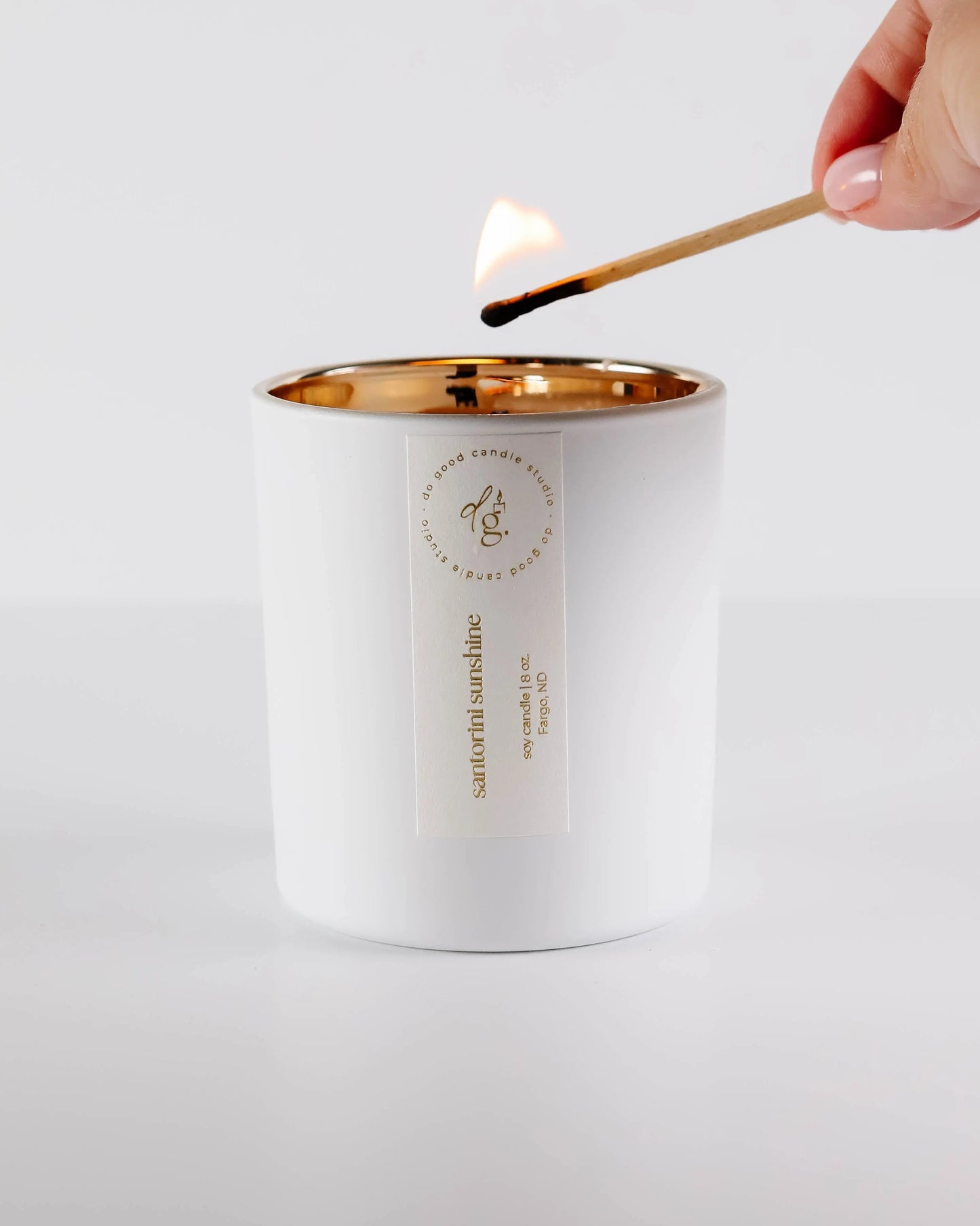 Santorini Sunshine candle being lit with candle on a white backdrop