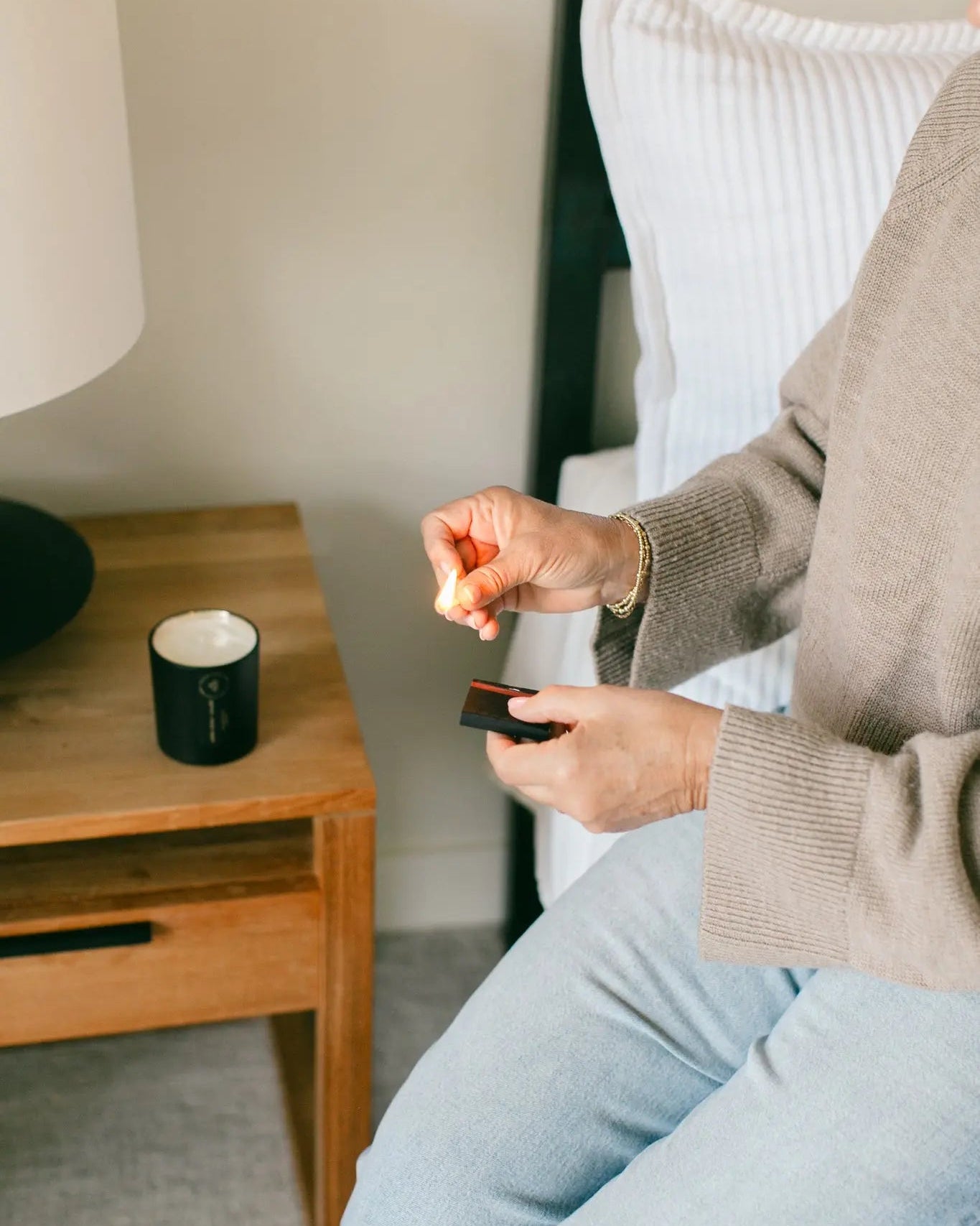 Woman ligting a Lavender Driftwood candle on a nightstand next to her bed