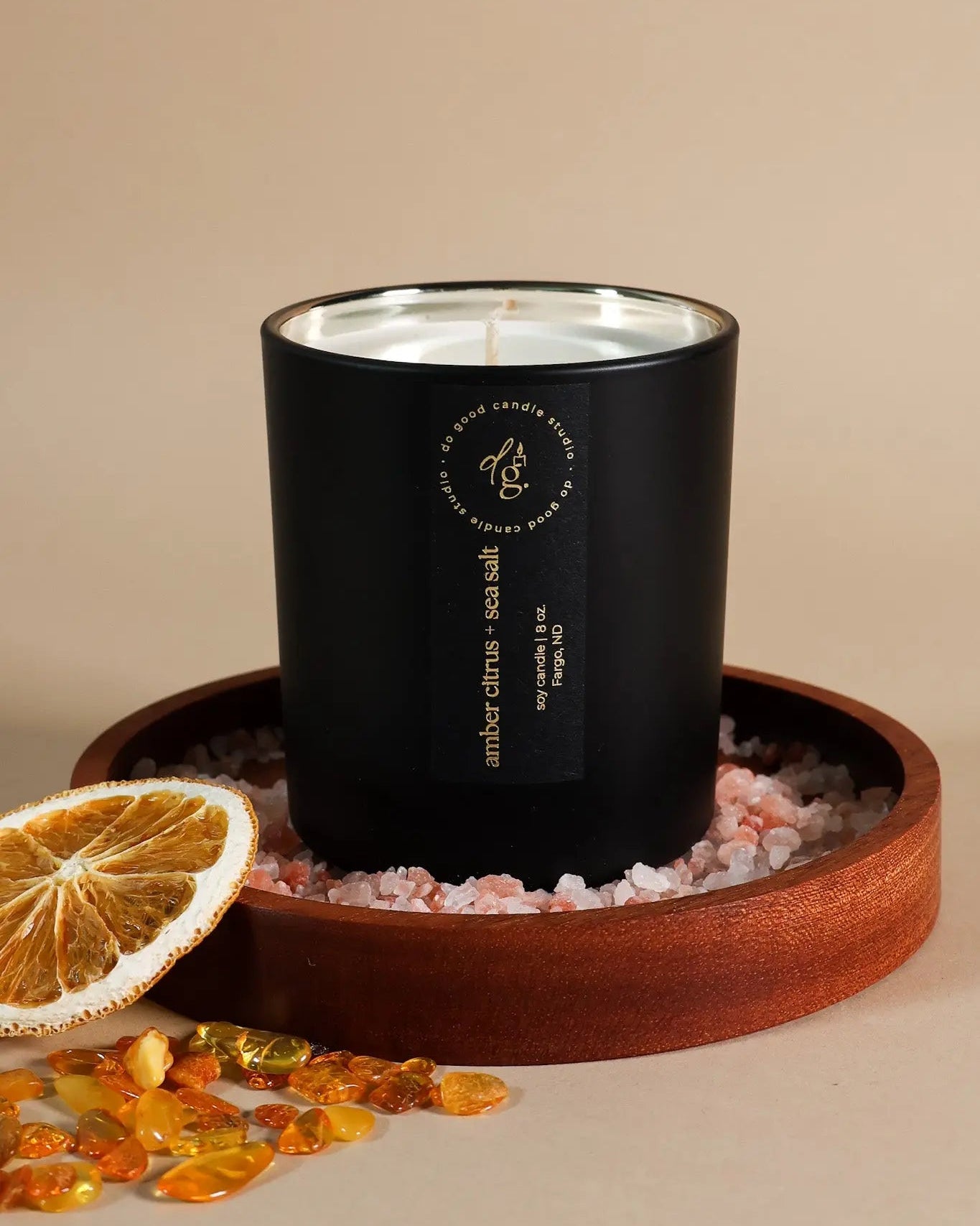 Soy candle in matte black vessel with black label on a wooden tray with decorative elements on a beige background