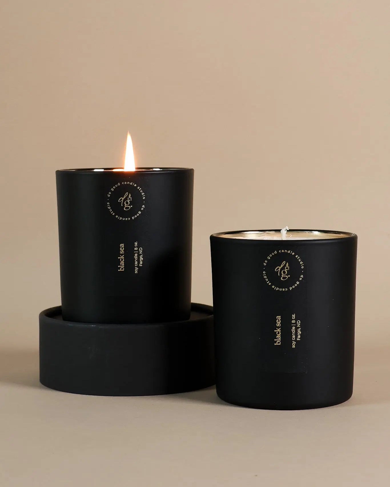 Two black candles with visible flames on a beige background