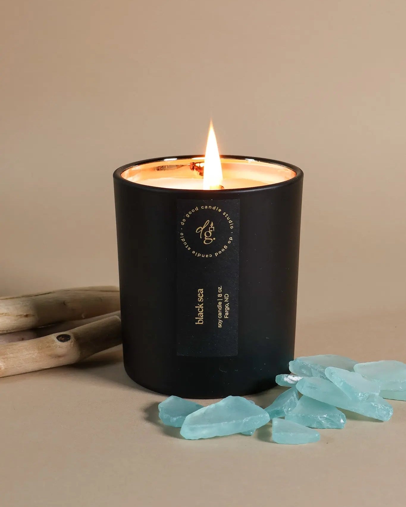 Black candle with a lit wick on a beige background, surrounded by decorative elements.