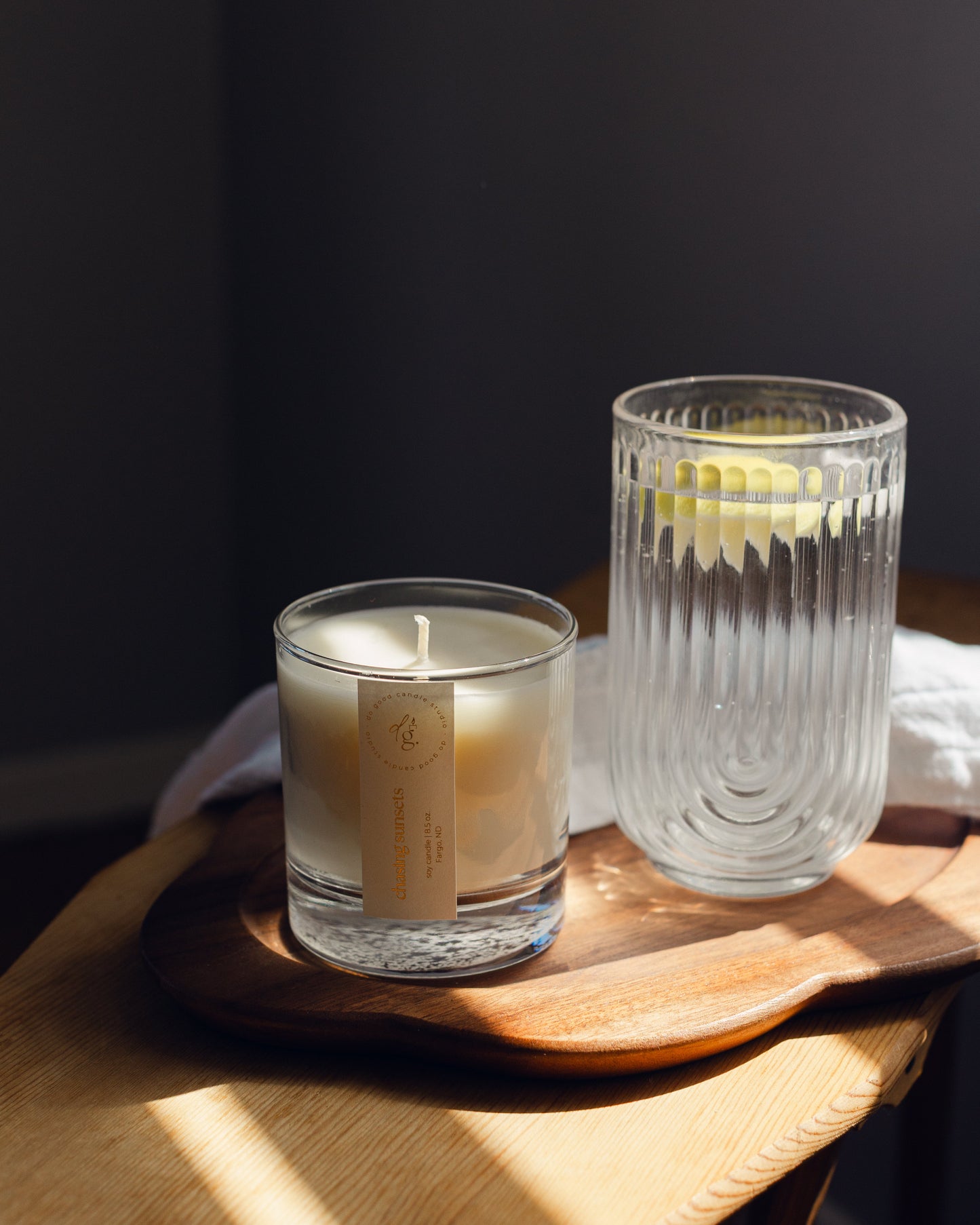 Chasing Sunsets candle on a wooden tray and golden sunlight with a glass of lemon water