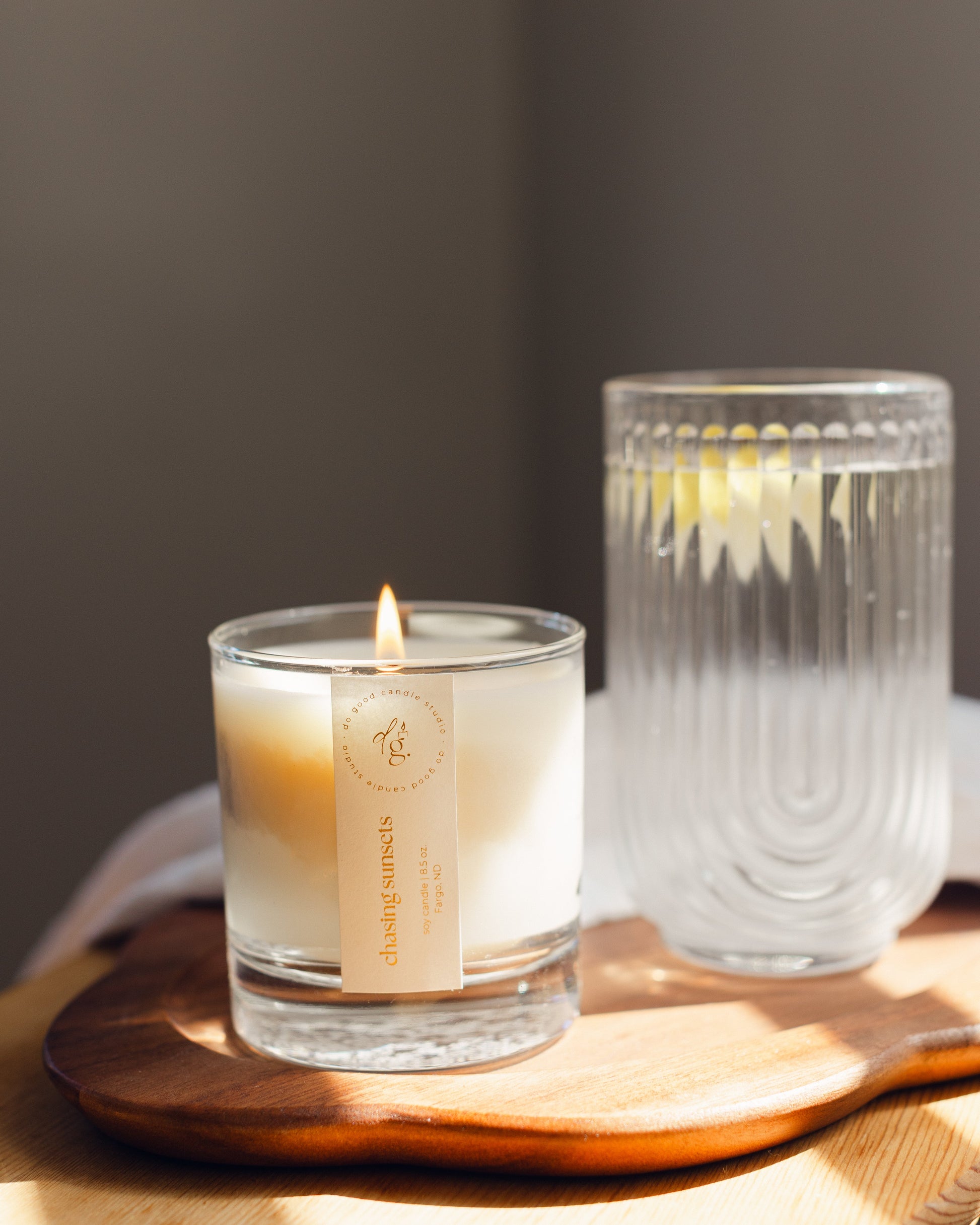 Chasing Sunsets candle burning on wooden tray with a glass of lemon water
