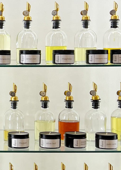 wall of fragrance oils in clear bottles with pour spouts and a same candle in front.