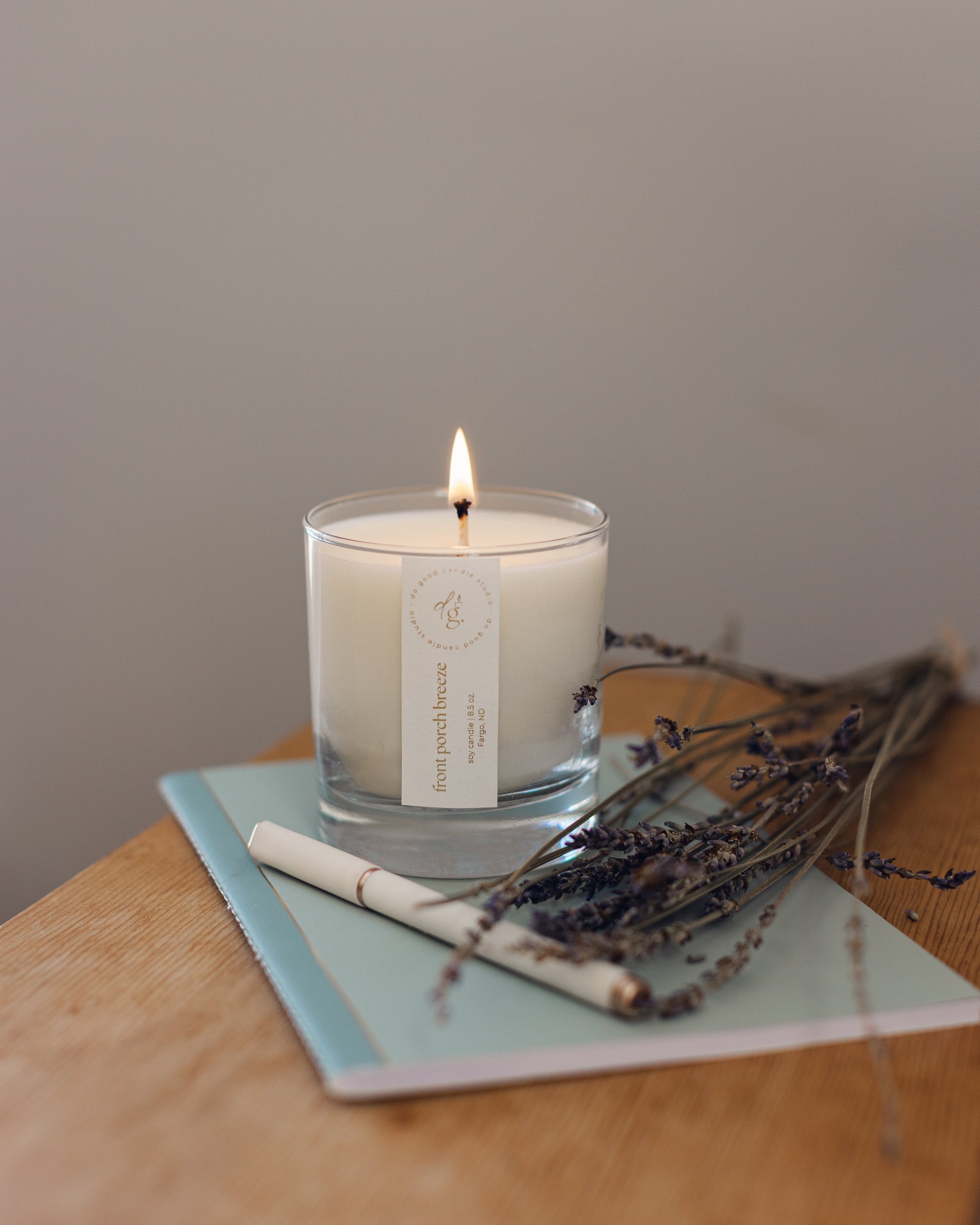 Front Porch Breeze candle burning while sitting on a blue journal with a pen and sprig of lavender