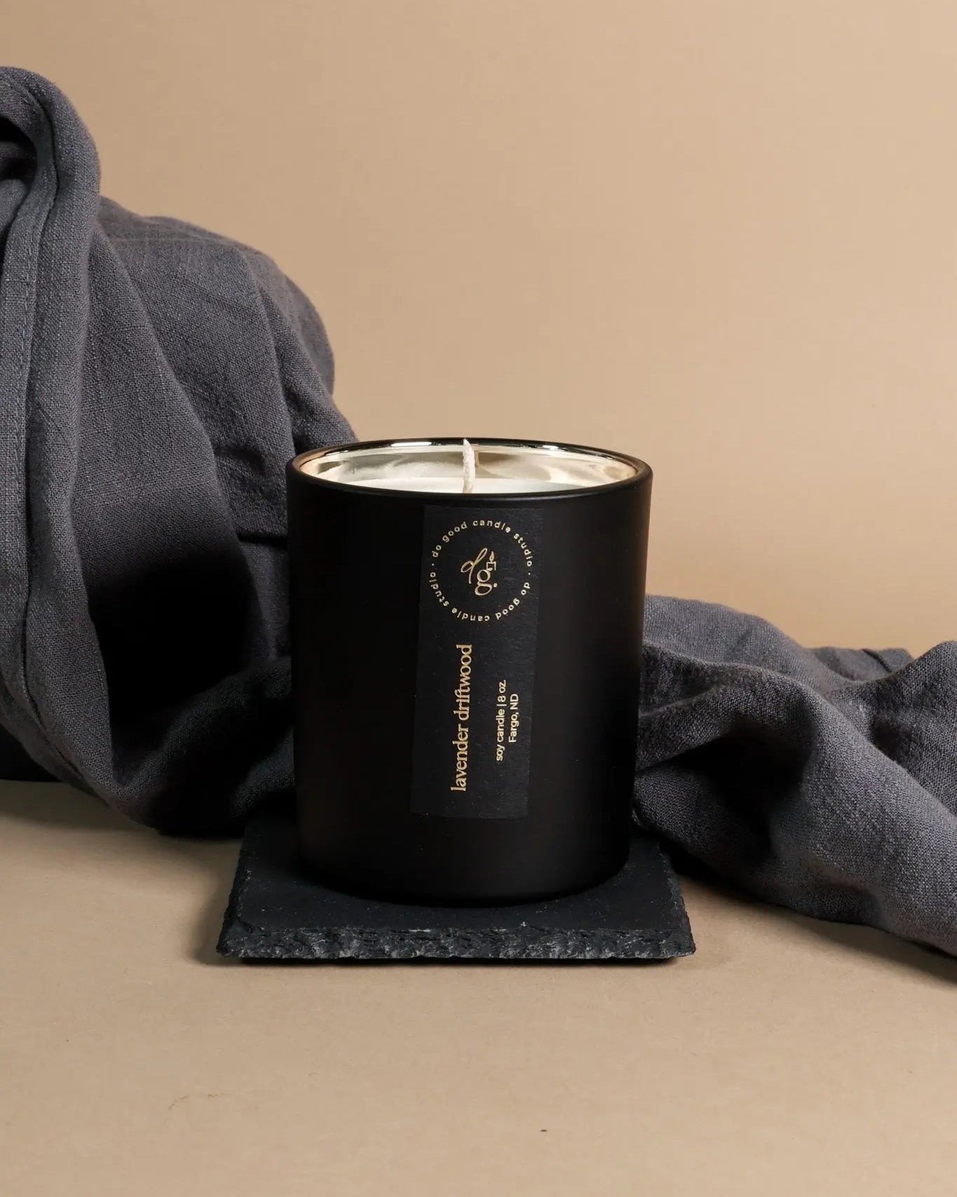 Lavender Driftwood candle styled on a beige background with a gray towel and slate coaster