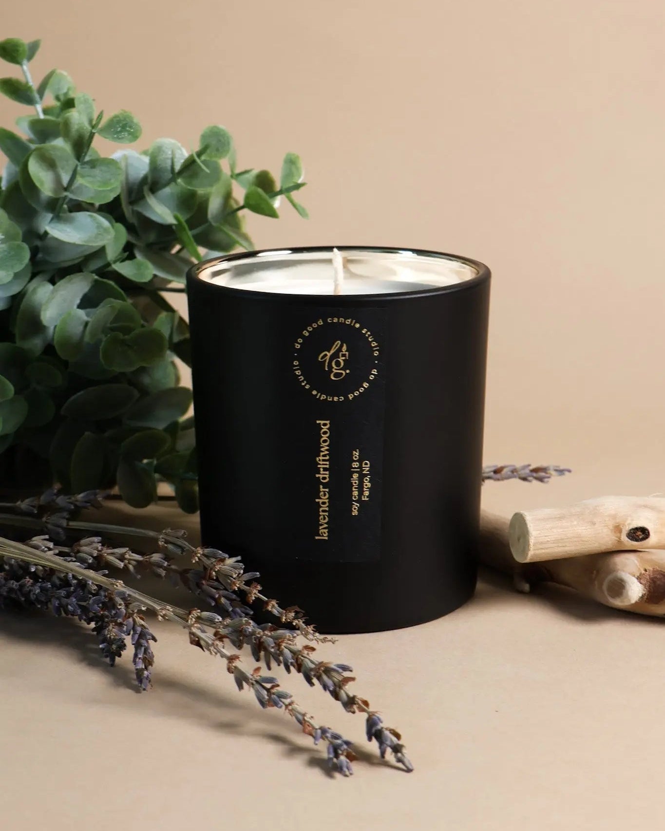Lavender Driftwood candle styled on a beige background with a plant , lavender sprig, and driftwood