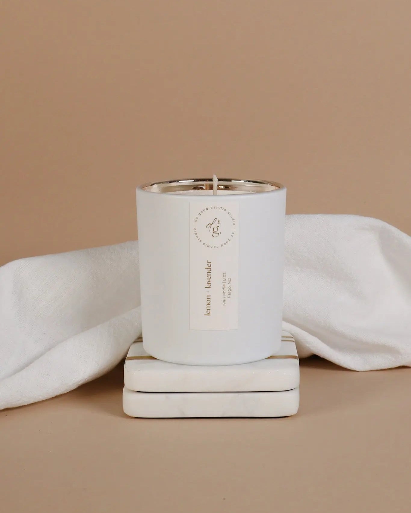 Lemon + Lavender cnandle styled on a beige backdrop with white coasters and a white linen cloth