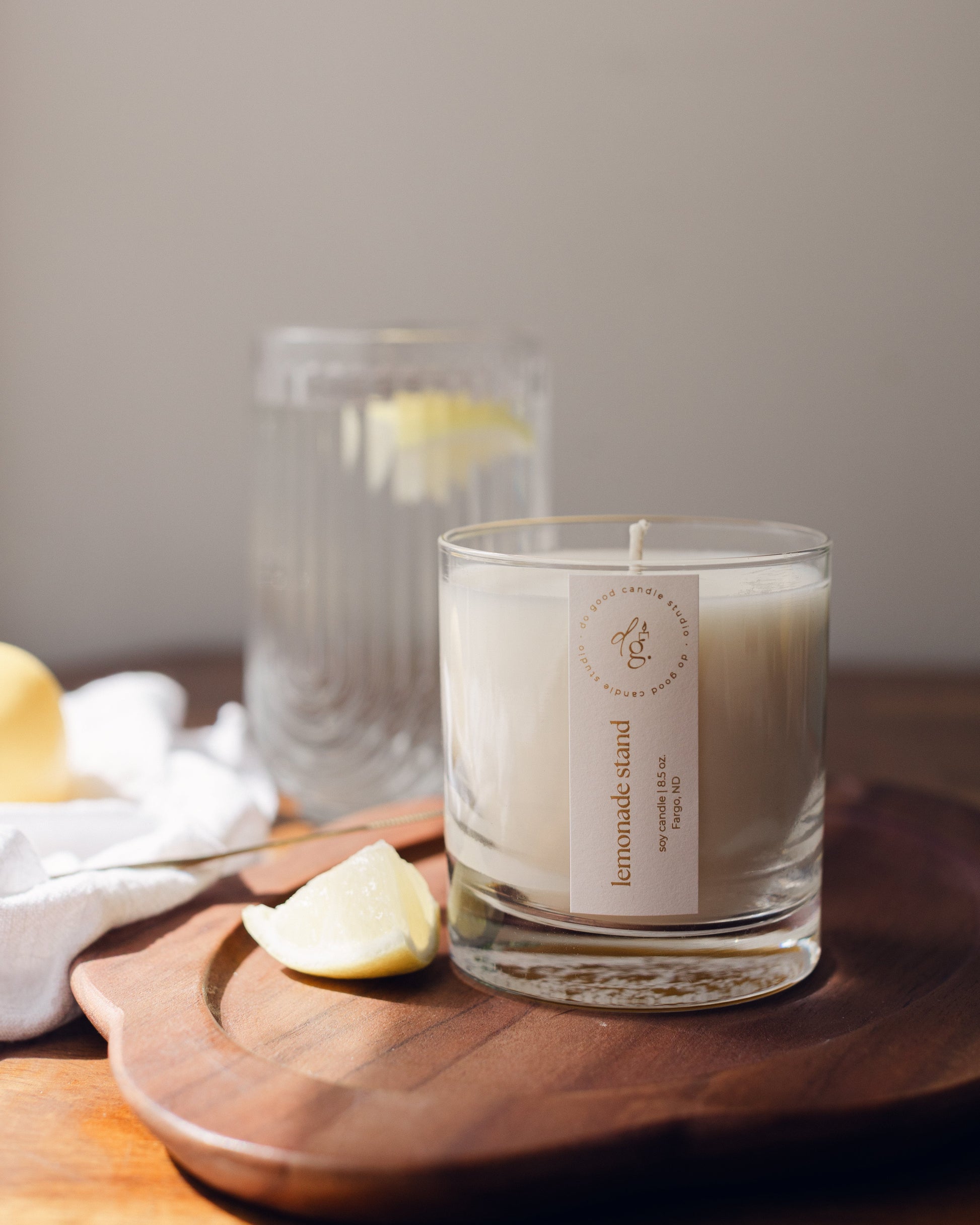 lemonade tand candle on wooden tray with lemon wedges and a glass of lemon water nearby