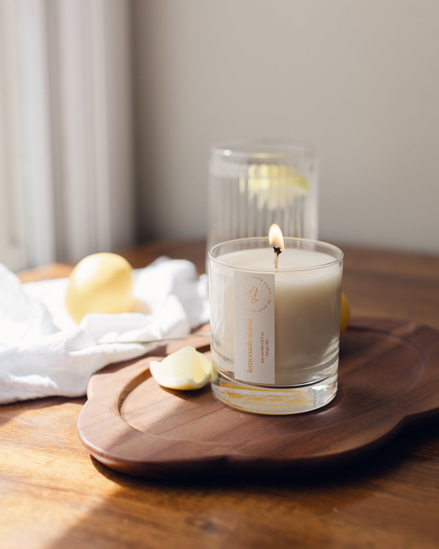 Lemonade Stand Candle burning on a wooden tray with lemon wedges and glass of lemon water nearby