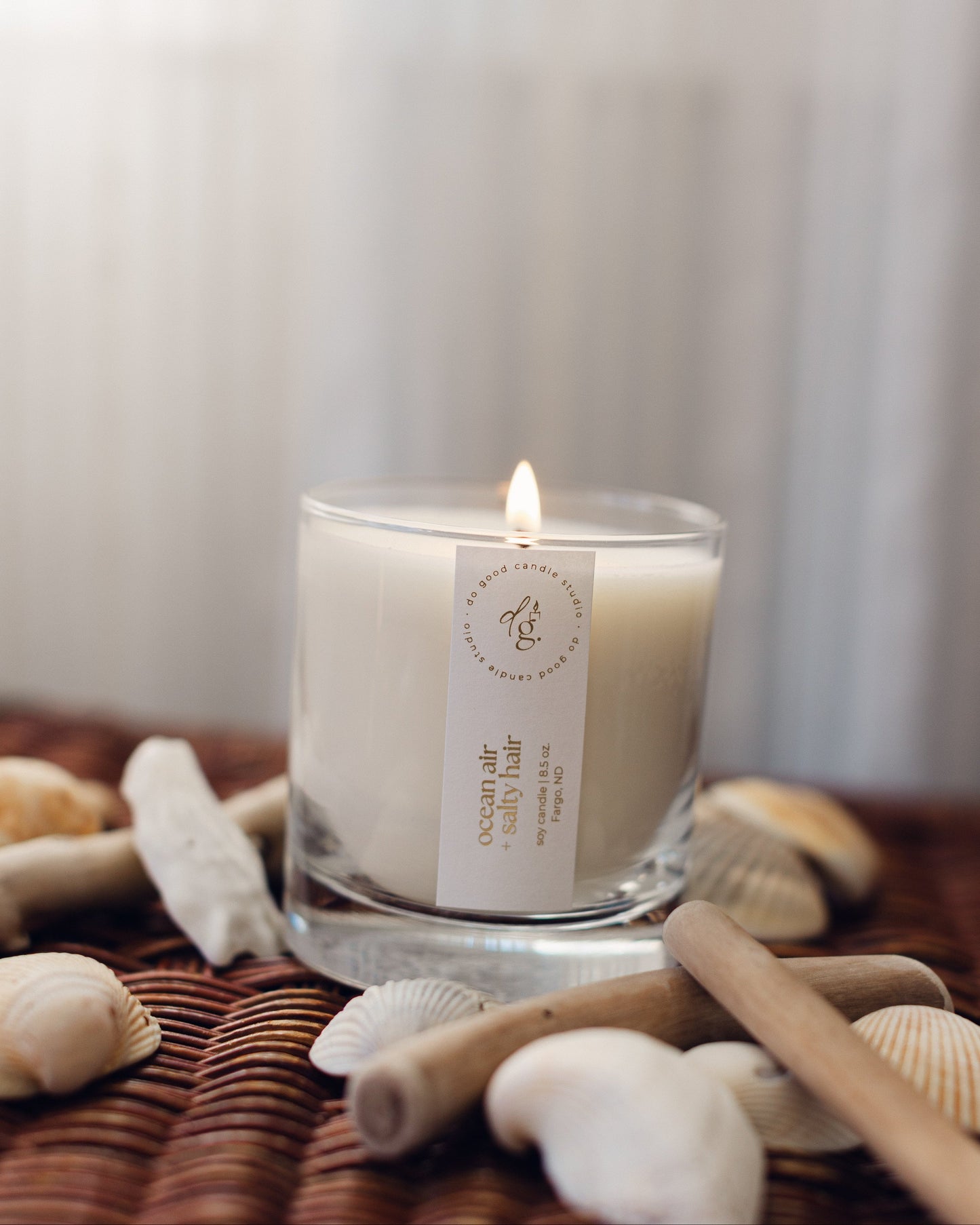 ocean air + salty hair candle burning on a wicker base with shells and driftwood