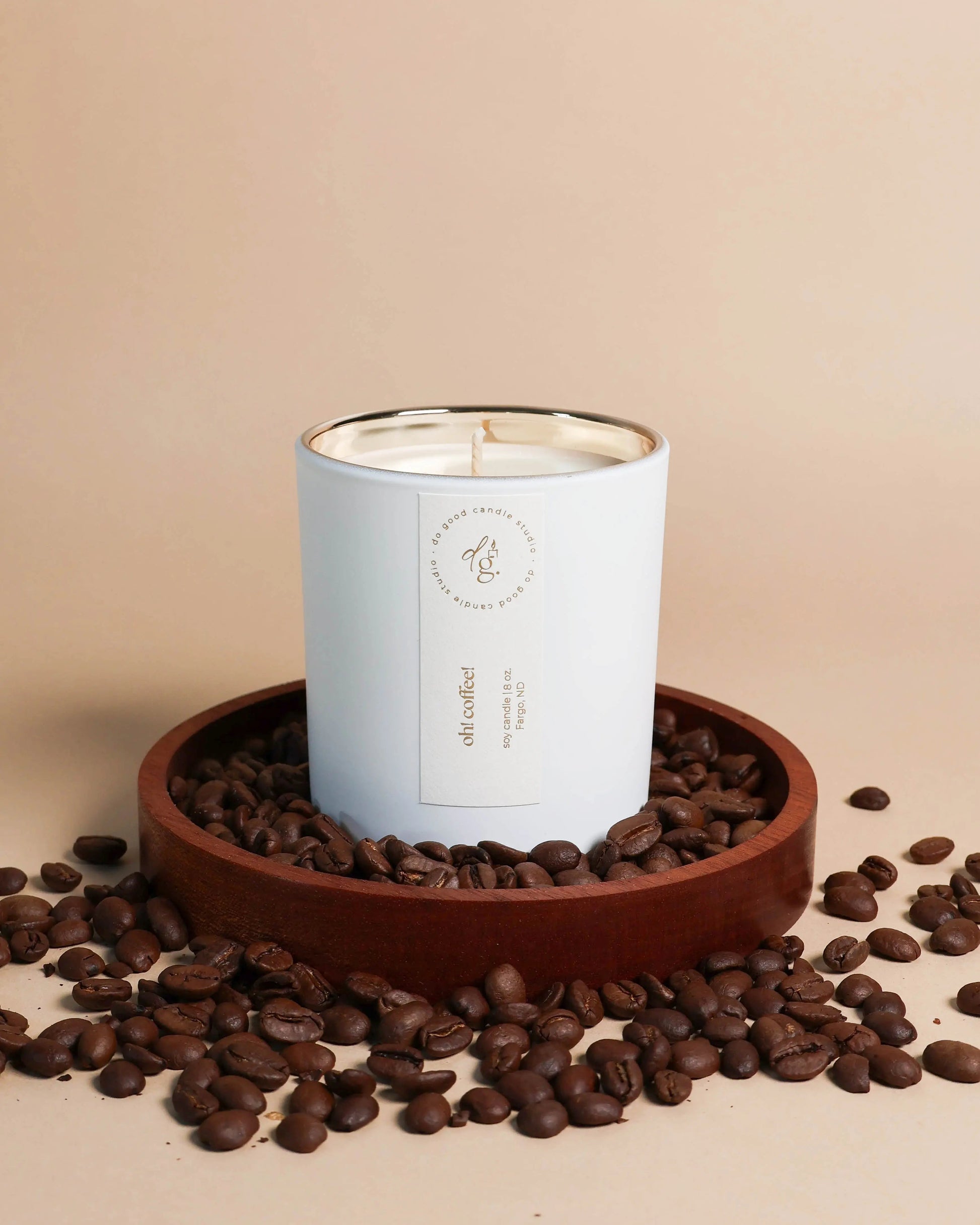 Oh! Coffee! candle styled on a beige backdrop with a wood coaster full of coffee beans